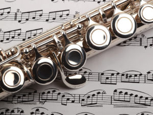 A used flute rests across an open msical score. Only one line of music is in focus.