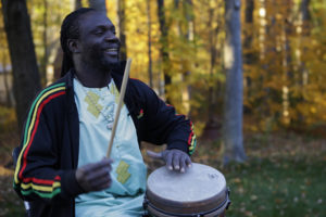 Photo of Diali Cissokho playing a drum and smiling