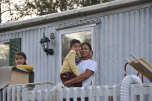 Photo from left to right- young girl, woman holding small boy, all watching Truck-and-Trailer from their porch