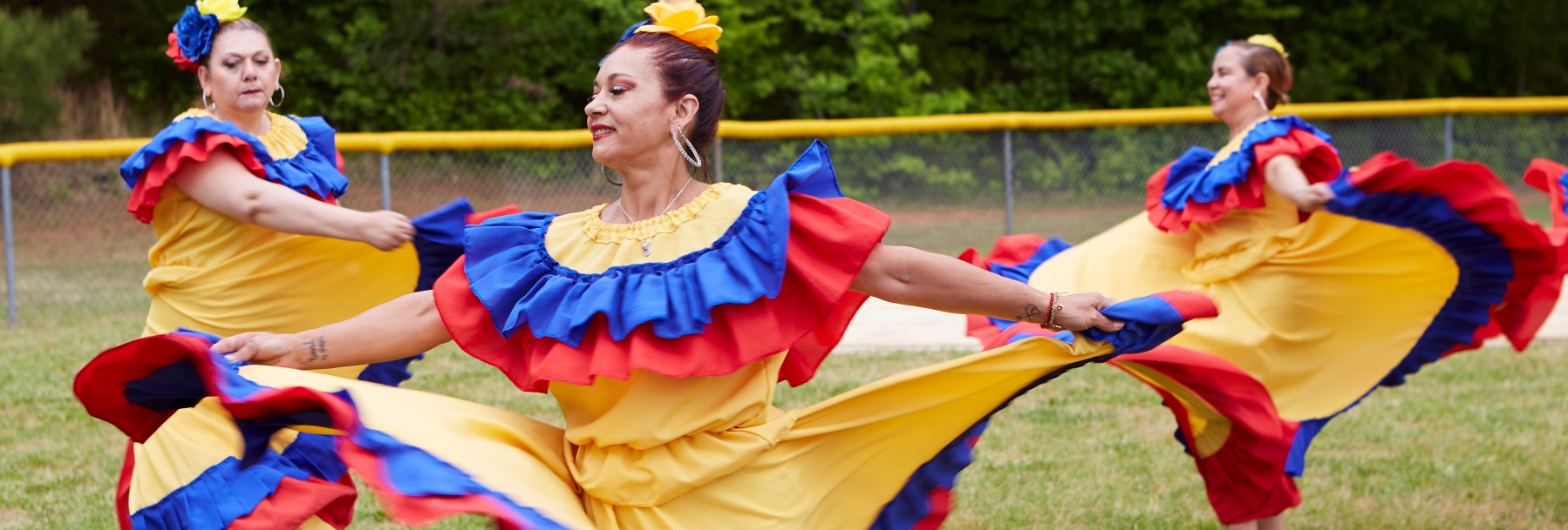 Photo of Latina women in brightly colored dresses dancing at ClydeFEST