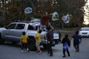Photo of truck with man in the bed, creating giant bubbles while a group of children follow behind