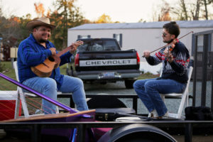 Photo of Larry & Joe on playing a guitar and fiddle on a trailer