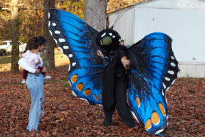 Giant butterfly costumed character interacts with a woman holding a baby