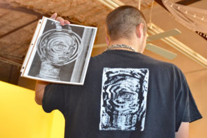 Photo of Caleb holding his original artwork next to a shirt it's printed on