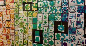 Patchwork of green, yellow, and blue student artwork hanging on the wall.