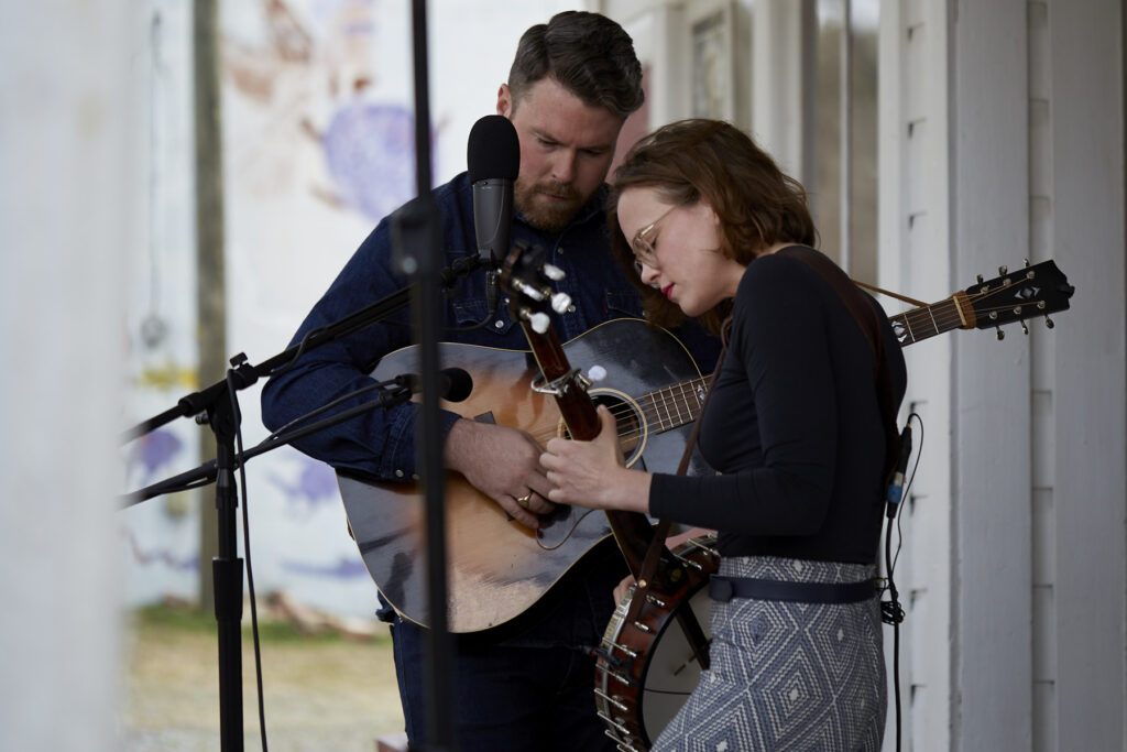 Photograph of roots duo the Chatham Rabbits, Austin is playing a guitar and Sarah is playing a banjo.