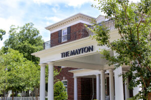 Photo featuring the entrance to The Mayton Inn. It is a brick building with a a large white awning supported by large white pillars