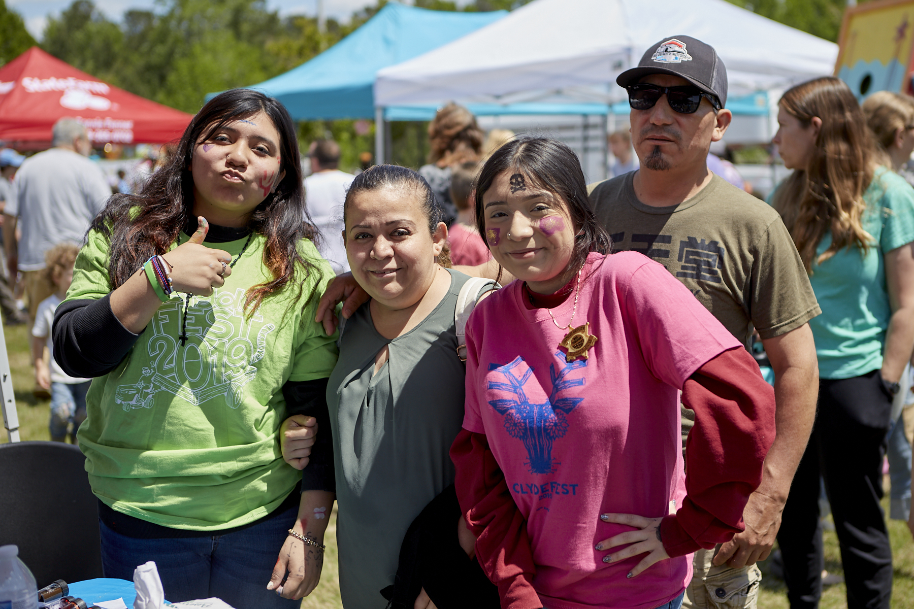 Photo of Latino family, L to R - teenage girl in green ClydeFEST shirt, woman with ponytail (mom), teenage girl in pink ClydeFEST shirt, man in baseball cap and sunglasses (dad)