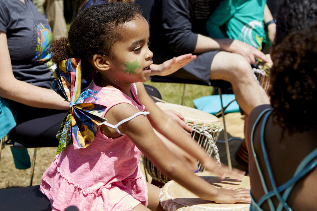 Girl with painted face and paper wings plays a drum