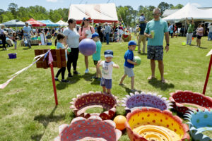 Photo of brightly painted tires and a child throwing a ball into them, while adults watch.
