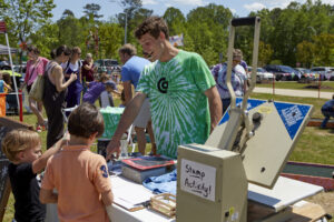 Photo of man in tie-dyed Chatham Arts Council shirt demonstrating print blocks to a child