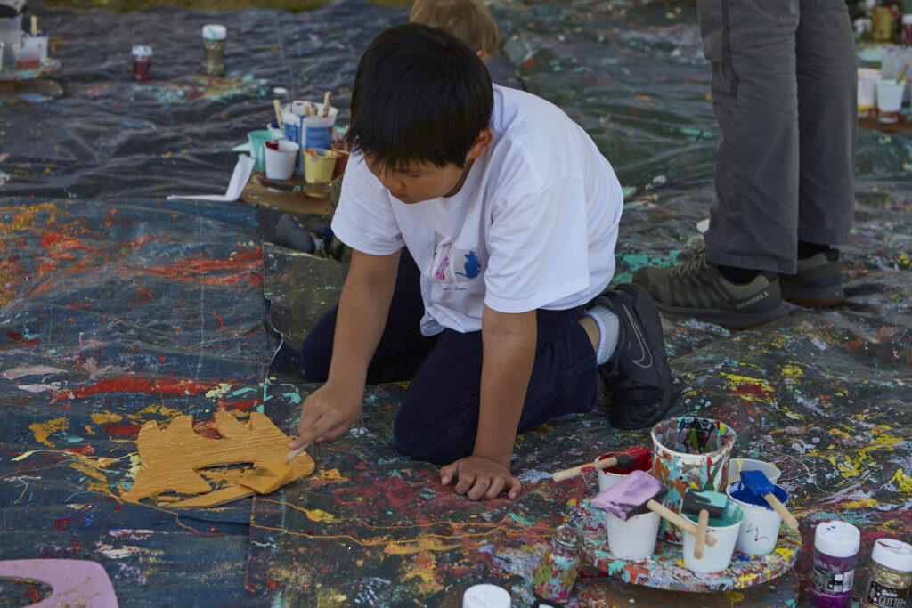 Photo of child on his knees painting his wooden critter cut-out a bright yellow