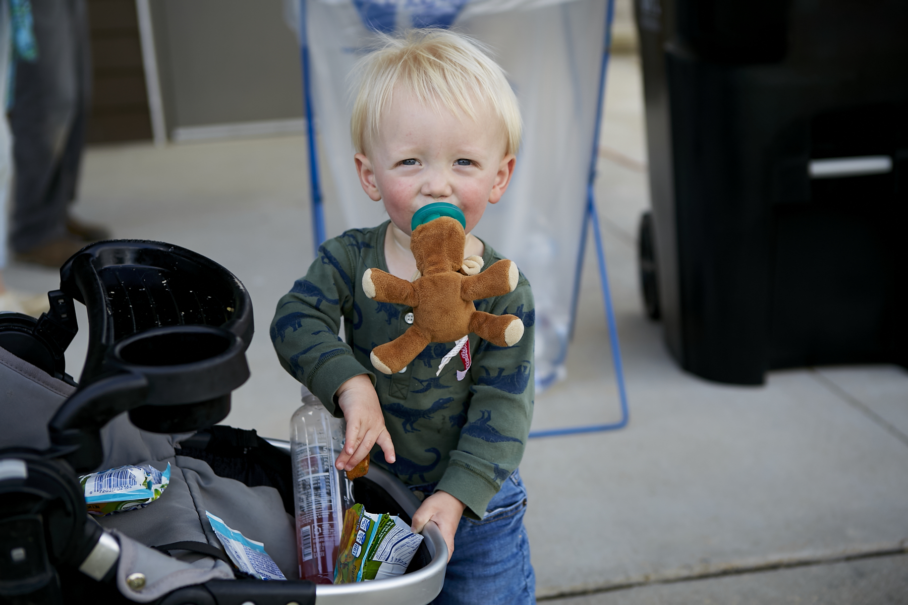 Photo of toddler boy with a pacifier in his mouth getting snacks from his stroller