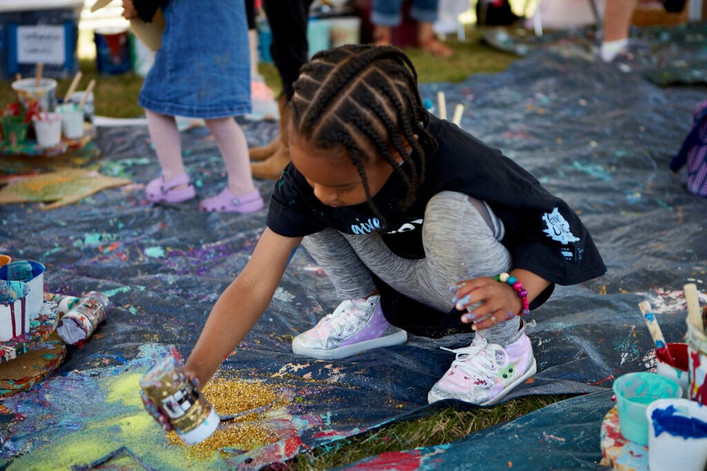Young girl squats on a tarp, pouring gold glitter onto her Clyde critter cut-out