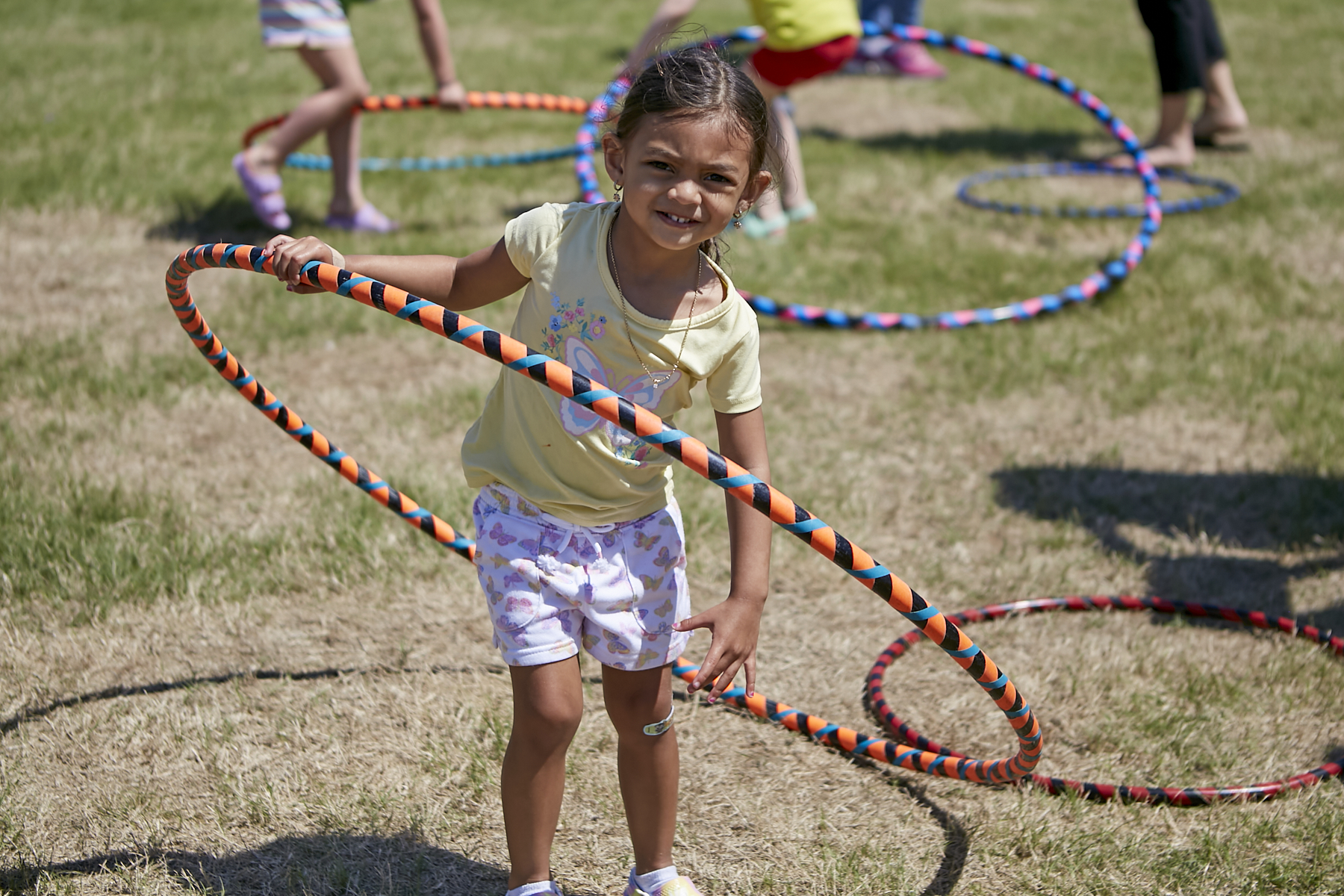 Photo of small girl with a ponytail and earrings, holding a large hula hoop