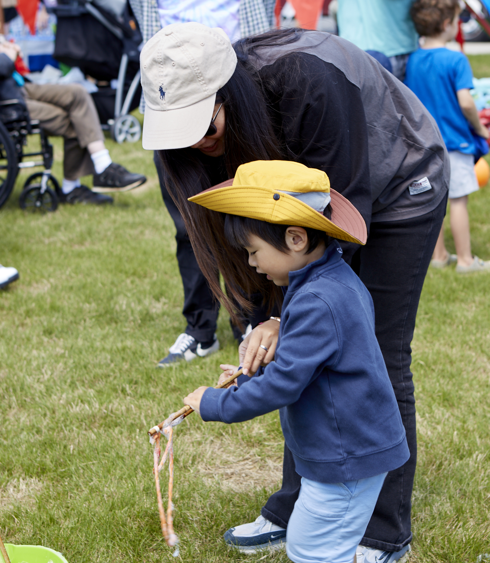 Woman in baseball hat assisting young boy wearing a sunhat with giant bubbles