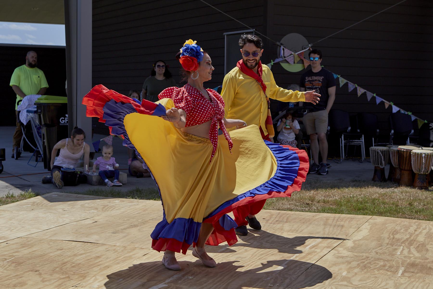 A man and woman, in brightly colored traditional costumes dance on a wooden dance floor; Takiri Folclor Latino