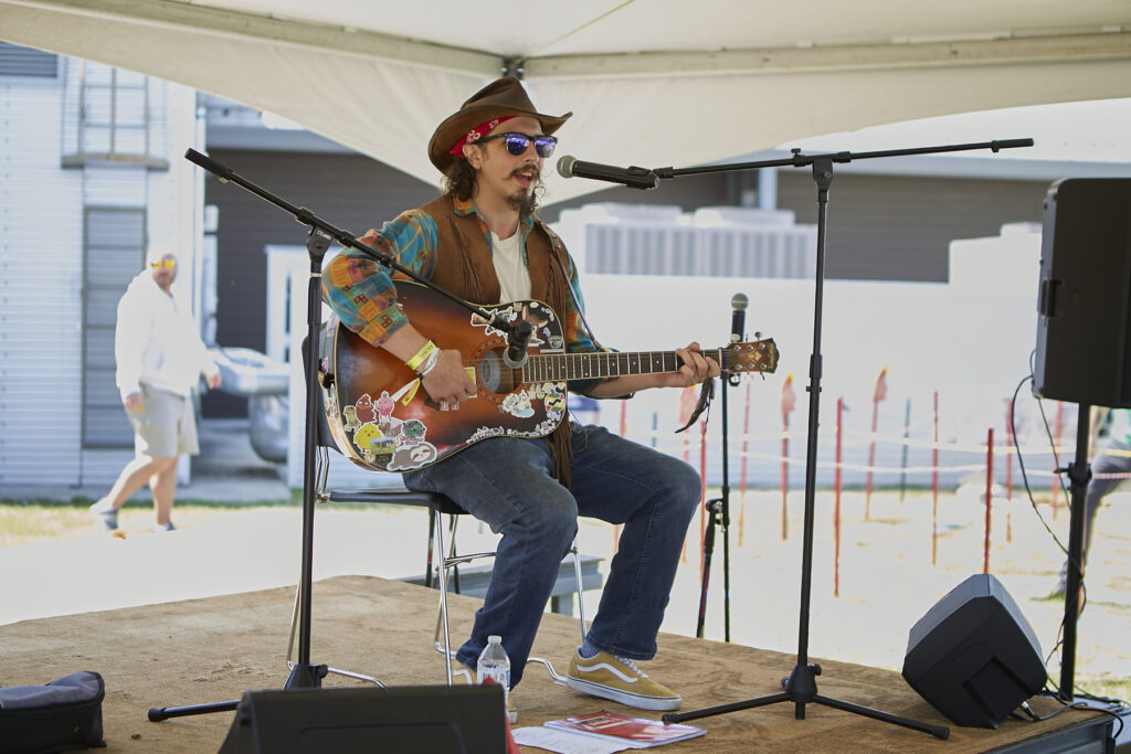 Photograph of man wearing a cowboy hat, sitting and playing guitar on the ClydeFEST 2023 stage
