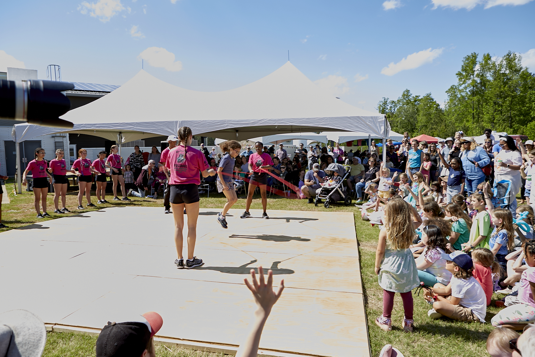 Photo of Bouncing Bulldogs team members turning two ropes while a girl from the audience jumps; audience members in the foreground and on the right have their hands raised to be the next jumper