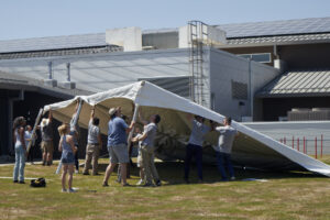 Photograph of people raising a big white tent.