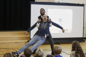 Photo of Mike Wiley catching a male teacher pretending to faint in performance of One Noble Journey
