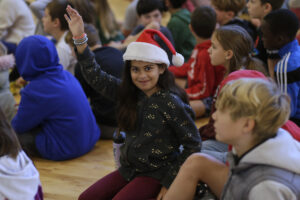 Photo of young girl wearing a Santa hat, raising her hand during the Q&A after the performance