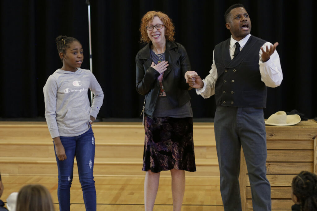 Photo of young girl, a teacher, and Mike Wiley in performance of One Noble Journey