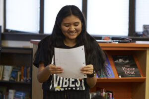 Photo of a teen girl standing and reading her story from a piece of paper she is holding.