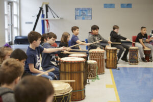Students sit behind African drums, playing them with drumsticks