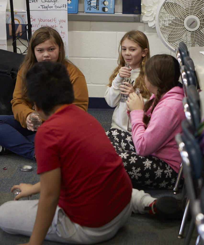 Four young students sitting on the floor playing their instruments made from recycled glass items