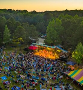 High overhead view of a large festival crowd gathered at an outdoor stage at sunset.