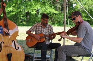 Three band members playing old-time music outside under a tent. Upright bass, guitar, and fiddle.