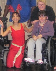 Three women--one in bright red clothes kneeling, one in a wheelchair, one behind the wheelchair.