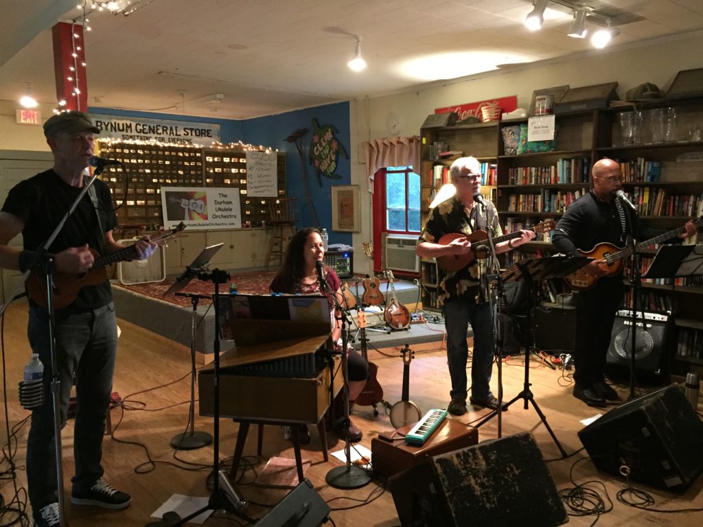 A band--three men and one woman--plays inside a general store with books on the walls, old signage, and smattering of musical instruments.