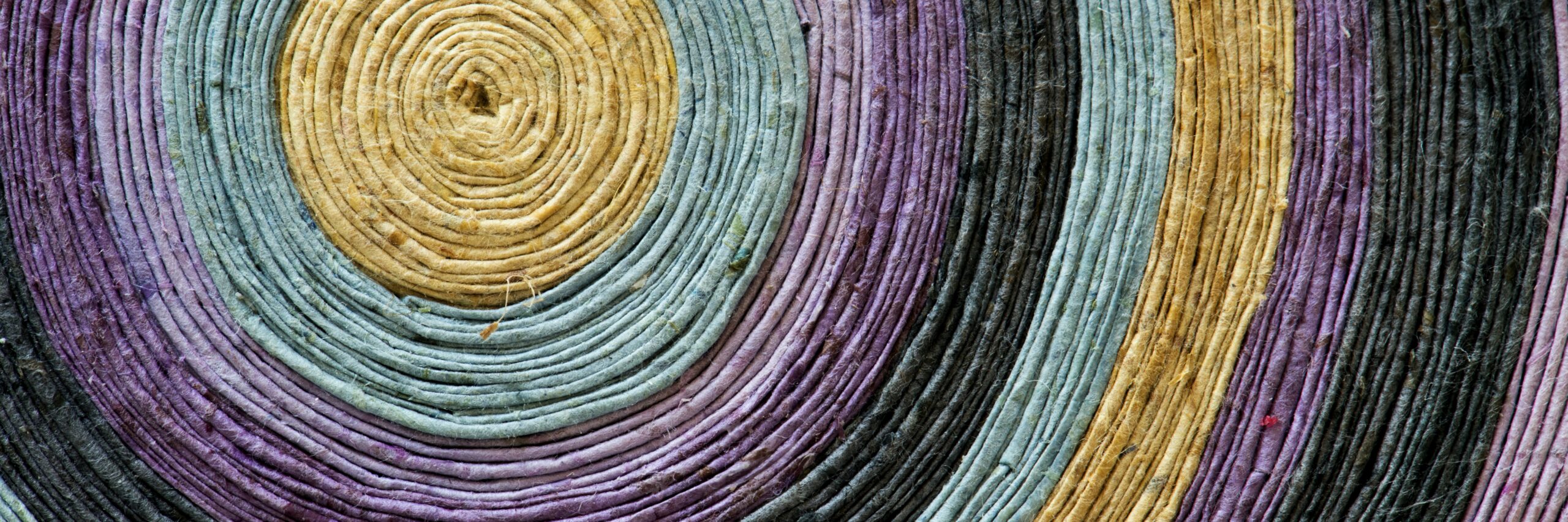 Close-up of textile art in a round shape. Colors include tan, blue, purple, black.