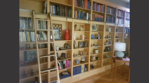 Custom wood book and art shelves covering a full wall, with a ladder for access.