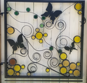 Metal and stained glass trellis featuring blue butterflies and yellow, green, and red abstract circle designs.
