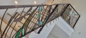 Stairwell with metal bannister featuring dragonflies with green stained glass.