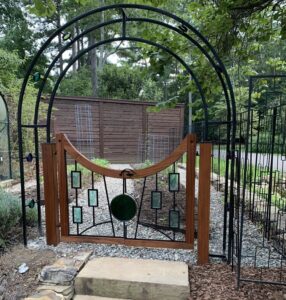 Wood, metal, and stained glass garden gate featuring overhead arch.