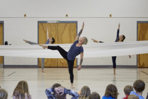 Photo of 3 female dancers from Black Box Dance Theatre dance with a white fabric to represent wind