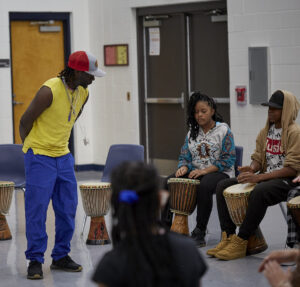 Photo of Diali Cissokho talking with students holding drums