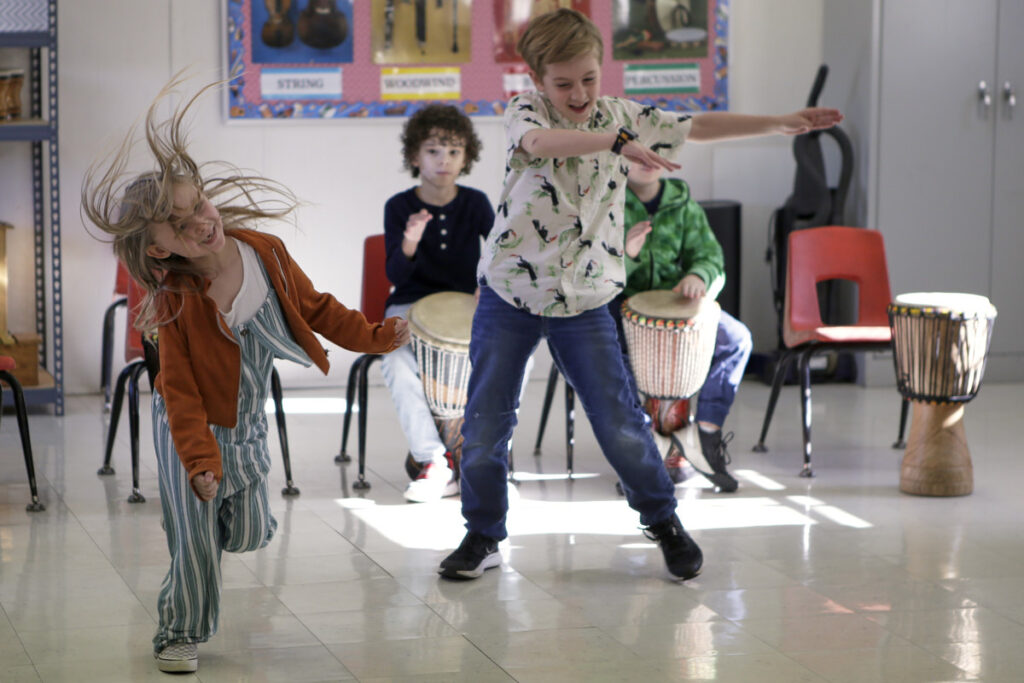 Two second grade students dance surrounded by classmates playing drums