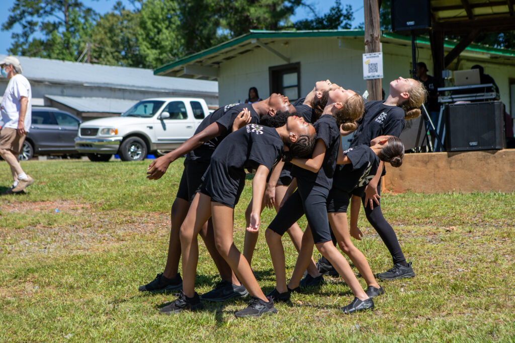 Group of young dancers dressed in all black, bending backwards in unison