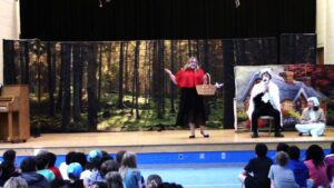 Actor on a stage performs as Little Red Riding Hood.
