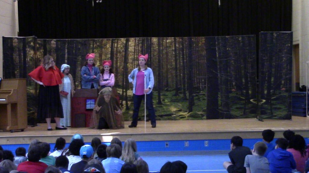 Actors on a stage costumed as the Three Little Pigs, Little Red Riding Hood, and the Grandmother.
