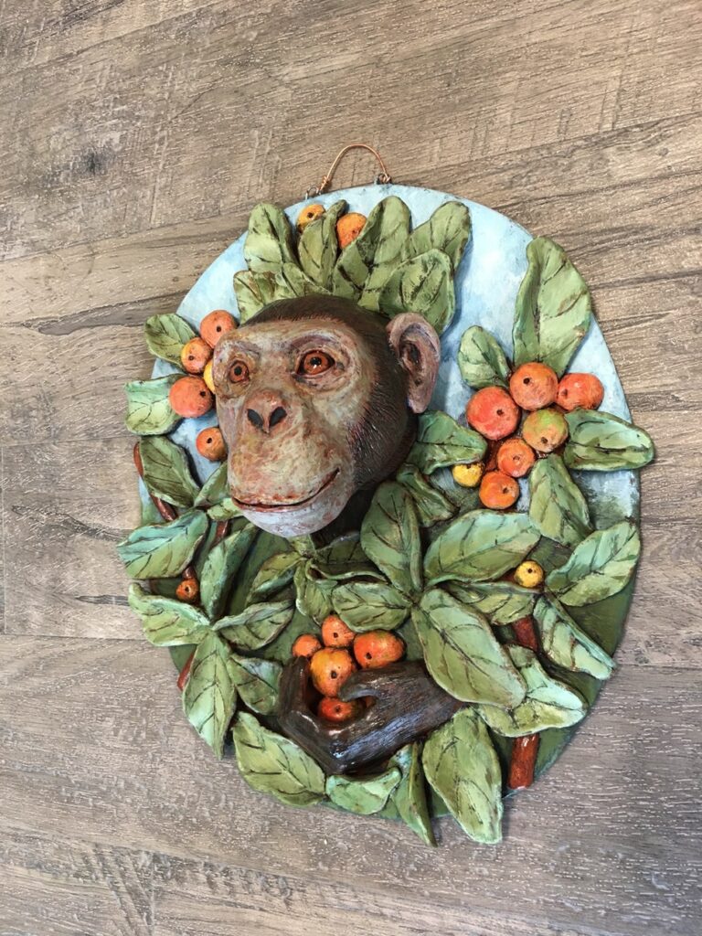 a clay wall hanging of a monkey head surrounded by orange fruits and leaves