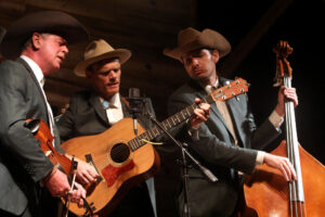 Three men in cowboy hats perform with guitars.