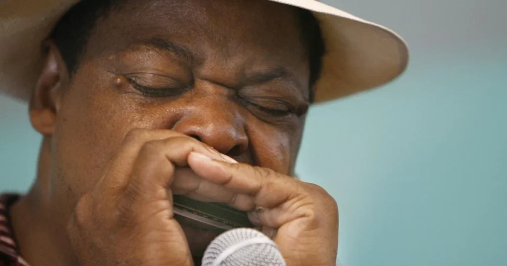A black man in a white hat playing harmonica 