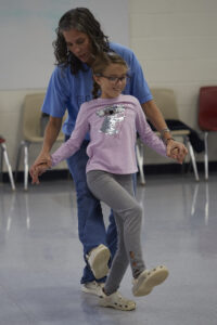 A student with mobility issues gets support from her adult teacher in order to participate in a dance routine.