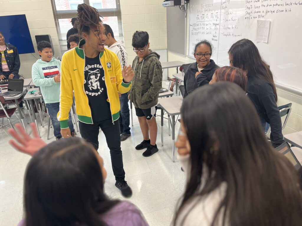 Students explore beat making with their bodies, led by Pierce Freelon, a Black man with a bun of dreadlocks